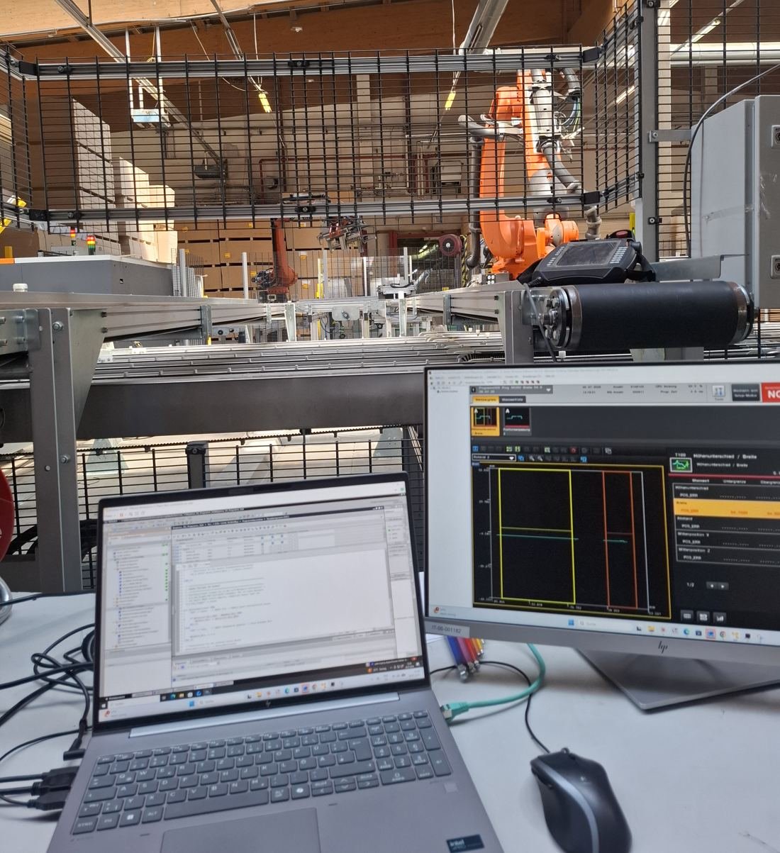 Laptop mit Steuerungssoftware und Monitor mit Bildverarbeitung vor einer Roboteranlage